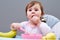 Adorable toddler girl is having fun while eating on greyish background