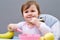 Adorable toddler girl is having fun while eating on greyish background