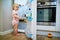 Adorable toddler girl at home, opening the fridge