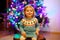 Adorable toddler girl sitting near Christmas tree. Little child playing and decorating xmas tree with family. First