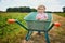 Adorable toddler girl in straw hat sitting in wheelbarrow on a farm