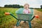 Adorable toddler girl in straw hat sitting in wheelbarrow on a farm