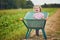 Adorable toddler girl in straw hat sitting in wheelbarrow on a farm