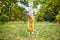 Adorable toddler girl in yellow dress having fun in park or forest and picking flowers