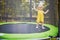 Adorable toddler girl in yellow dress having fun on a trampoline on a summer day