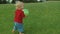 Adorable toddler going on green field barefoot. Boy holding ball in hands