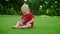 Adorable toddler holding cellphone in hands. Cheerful boy sitting on green grass