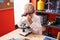 Adorable toddler student using microscope standing at classroom