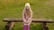 Adorable unhappy girl sitting on wooden bench on green grass