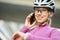 Adorable young female cyclist wearing protective helmet and glasses smiling at camera while talking on the phone