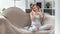 Adorable young female relaxing at sofa listening music wearing headphones using smartphone