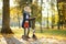 Adorable young girl riding her scooter in a city park on sunny autumn evening. Pretty preteen child riding a roller