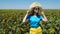 Adorable young girl in a straw hat, yellow skirt and blue t-shirt in sunflowers field. Lady with long blonde hair 4K