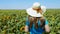 Adorable young girl in a straw hat, yellow skirt and blue t-shirt in sunflowers field. Lady with long blonde hair 4K