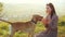 Adorable young woman playing with dog and feeding it on nature