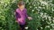 Adorable youth girl walking in green field with white chamomile flowers