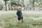 Adorably Happy and Cute Little Caucasian Toddler Baby Boy with Long Blond Hair Laughing, Playing, and Running Outside in Green Nat