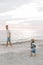 Adorably Perfect Young Father and Baby Toddler Son Family Having Fun Time at the Sandy Beach During Sunset Outside By the Ocean Wa