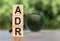 ADR Abbreviation On Wooden  Blocks on table with magnifier on green background