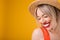 Adrable smiling confused embarrassed modest blonde woman in straw hat. Warm summer mood yellow background. Lovely happy