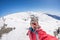 Adult alpin skier with beard, sunglasses and hat, taking selfie on snowy slope in the beautiful italian Alps with clear blue sky.