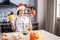 Adult attractive woman stand in kitchen and posing on camera. Holding peppers in hands. Wear red festive hat