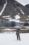 Adult backpacker standing on snow patch while hiking in mountains, mountaineering with backpack, mountain lake landscape with