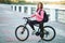 Adult beautiful redhead woman with bob haircut thinking drinking morning coffee posing on bicycle in autumn city river pier