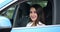Adult black-haired woman driver sits in blue car smiling