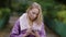 Adult blonde businesswoman is standing alone in park and typing message on her smartphone in daytime