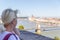 Adult blonde tourist in a white T-shirt with a crimson rucksack looks at the panorama of the old city. Budapest