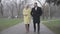 Adult Caucasian couple strolling in park in cloudy day. Blond woman in yellow coat and brunette man in elegant outfit