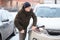 An adult Caucasian man with snow brush in hand clearing his car in winter season, swiping snow from headlight