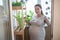 Adult Caucasian pregnant woman watering her small garden at home balcony