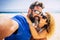 Adult couple of tourist take selfie picture at the beach with sand and blue ocean and sky in background. Hapy man and woman