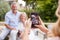 Adult Daughter Taking Picture Of Senior Parents Sitting In Garden On Mobile Phone