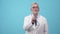 An adult doctor pretends to listen with stethoscope in the studio, a blue background. Man doctor in a robe and tie