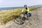 Adult female cyclist rides alongocean shore..