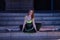 Adult female Hispanic classical ballet dancer in green and black tutu with coins, legs wide open in the middle of stairs