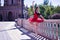 Adult female Hispanic classical ballet dancer in red tutu doing figures next to a stone railing in the middle of a plaza on a