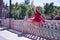 Adult female Hispanic classical ballet dancer in red tutu doing figures next to a stone railing in the middle of a plaza on a