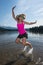 An adult female jumps in a lake, splashing water behind her feet on a summer day in California, near Mount Shasta