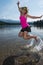 An adult female jumps in a lake, splashing water behind her feet on a summer day in California, near Mount Shasta