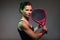 Adult fitness woman looking at camera while playing padel indoor. Isolated on black.