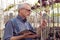 Adult gardener inspects plant diseases. The hands holding the tablet. In the glasses, a beard, wearing overalls. In the garden