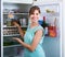 Adult girl arranging space of fridge shelves indoors