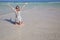 An adult girl kneels in the sea, arms outstretched.