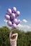 adult girl stands with her back with a bunch of purple helium balloons against the sky