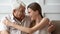 Adult granddaughter and old grandfather embracing sitting on couch indoors