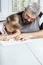 Adult gray-haired father teaches little daughter to write at the table at home